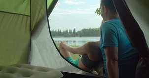 Happy traveler couple sitting near tent camp around mountains lake and shoot with her phone camera under sun light enjoying the leisure and freedom. 4K slow motion video

