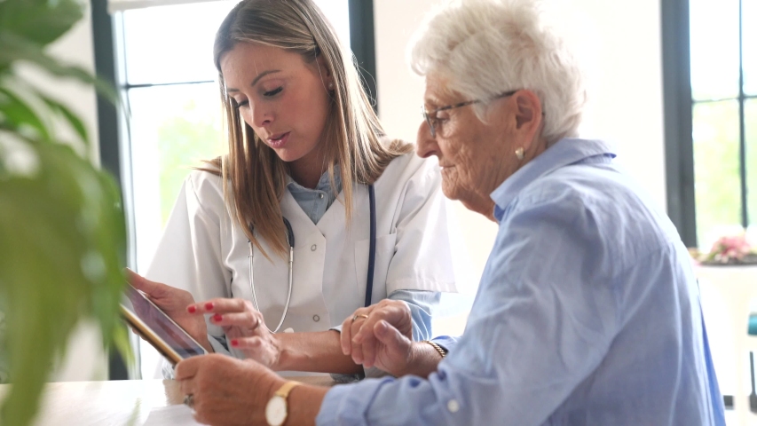 Elderly woman with nurse at home looking at tablet | Shutterstock HD Video #1038248240