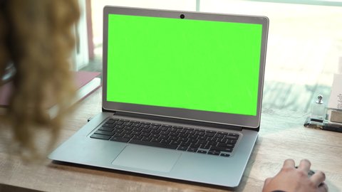 Laptop on a desk with a green screen over woman's shoulder