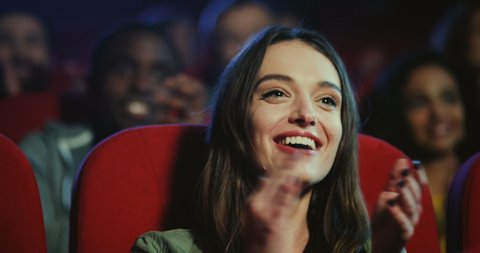 Portrait shot of the cheerful young Caucasian beautiful woman watching comedy film in the cinema, laughing and clapping hands.