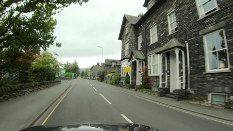 WINDERMERE, ENGLAND - 7 SEP 2019: England Lake District town drive POV. Historic old stone and rock homes along narrow winding roads. Hills, valley and mountain region.