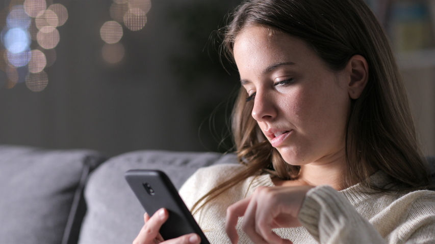 Bored woman reading smart phone content sitting on a couch in the night at home Royalty-Free Stock Footage #1038263348