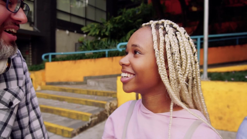 Black woman with braids in hair meets friend and gives tight hug. Warm welcome, very friendly and affable. Cheerful, happy youth moment. 
