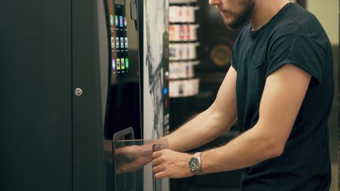 Young Man Drinking Coffee or Tea from Vending Machine