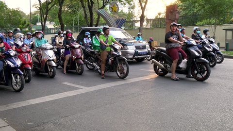 PEOPLE ON MOPEDS WAITING AT TRAFFIC LIGHTS ON THE STREETS OF HO CHI MINH CITY OR SAIGON, VIETNAM – 11 APRIL 2018: Scooters, mopeds, motorcycles, cars, traffic and people, Ho Chi Minh City, Vietnam