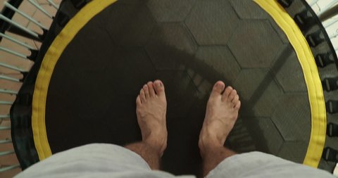 High angle point of view of man bouncing on small trampoline with focus on feet