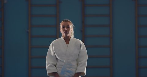 Pretty woman fighter is preparing for the competition. Girl stands on the tatami with bare feet in a white kimono. Top-down camera view.