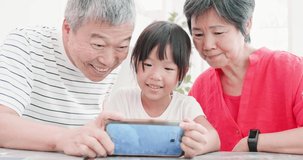 asian grandparents watch video on the smartphone with their granddaughter