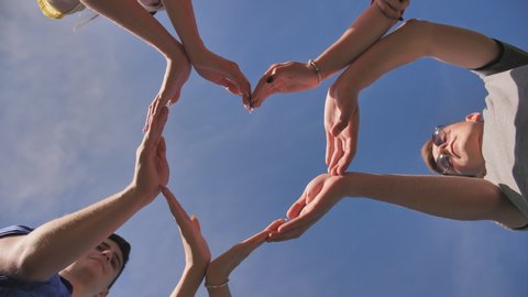 A group of friends makes a heart shape out of their hands.