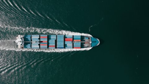 Aerial shot illustrating the process of ship transportation in Port Miami, USA. Cargo ship moves evenly on the water surface. Many containers loaded on the deck.