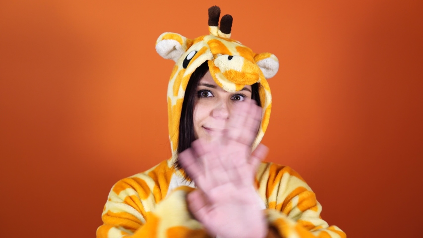 A funny woman in a big kigurumi of giraffe shows a stop sign which expressing protest on an orange background in the studio. Royalty-Free Stock Footage #1038309581