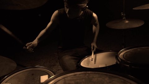 Teenager rock band drummer . cool and talented Asian American mixed young boy playing drums in headband performing song in dark background feeling super star on stage
