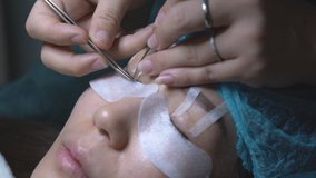 Eyelash extension and gluing artificial eyelashes with tweezers for Asian woman eye, slow down footage
