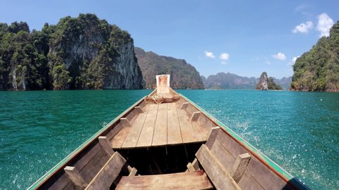 4K Nose of wooden motorboat view, vessel sailing on Thai Khao Sok Lake with foresty mountains around