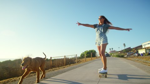 Young happy girl skateboarding with dog at sunset