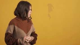 Upset worried brunette girl in knitted sweater looking aside and sadly waving no gesture on camera over yellow background