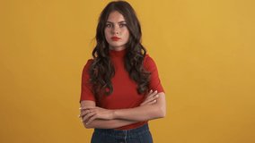 Serious brunette girl in red top confidently showing no gesture on camera over yellow background. No expression