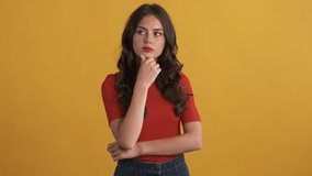 Beautiful pensive brunette girl in red top thoughtfully looking around over yellow background. Thinking expression