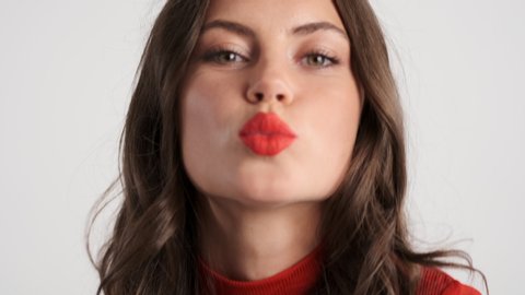 Portrait of beautiful flirty brunette girl charmingly sending kiss on camera over gray background
