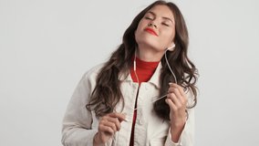 Beautiful casual brunette girl listening music in earphones dreamily dancing over gray background