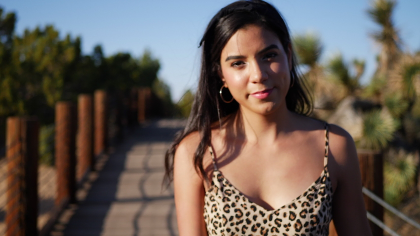 An attractive young hispanic woman traveler walking and smiling on a nature path in slow motion in sunset light.