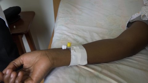Close up of an African woman's hand with a cannula in it and a doctor injecting medicine into her arm.