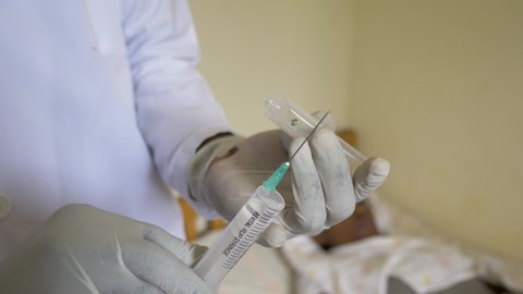 A close up shot of a African doctor wearing gloves preparing medicine into a needle in Africa.