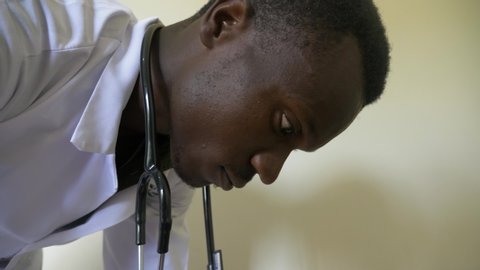A close up of the face of a young African medical practitioner as he concentrates on treating a patient.