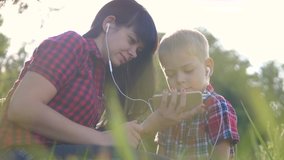 happy family funny video play music slow motion teamwork outdoors. Mom and son listen to music on smartphone in the same headphones for two. happy family mother woman and son little boy spend time in