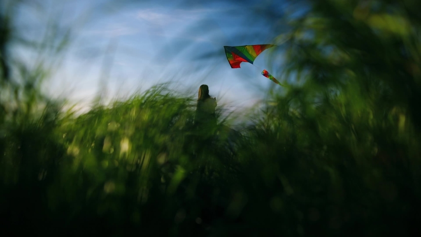 Beautiful girl in long white dress with kite standing on top of a mountain among tall green grass