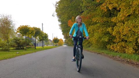woman on a bicycle rides on a country road in autumn, smiling.