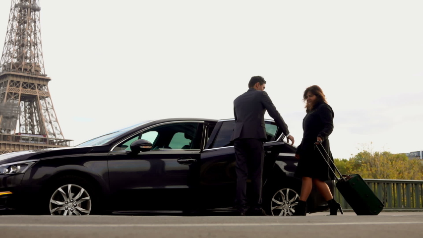 Personal driver is opening the car door for his client. Business women with a suitcase goes and sits into the car next to the Eiffel Tower. Hotel transfer services | Shutterstock HD Video #1038354380