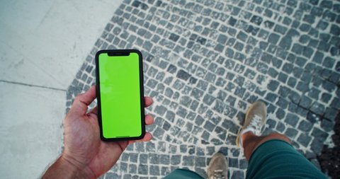 Lviv, Ukraine - August 27, 2019: Close-up young man browsing social network in smartphone green mock-up blank screen walking outdoors in the street.