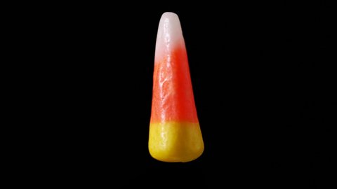 A single piece of candy corn is seen slowly rotating. The candy corn appears as if its floating and zooming back and forth to the camera.