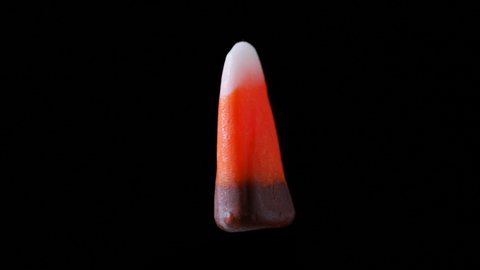 A piece of candy corn is seen floating and rotating. It is seen zooming in and out from the camera.