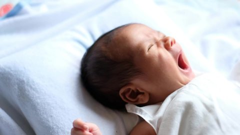 Newborn baby waking up and opening eyes. Lovely asian new born baby. Little baby boy lying on bed. Concept of caring for children and parental love.