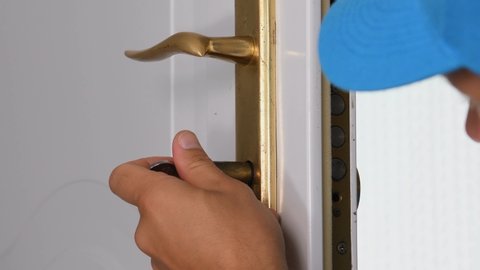 Locksmith installing door lock with screwdriver.