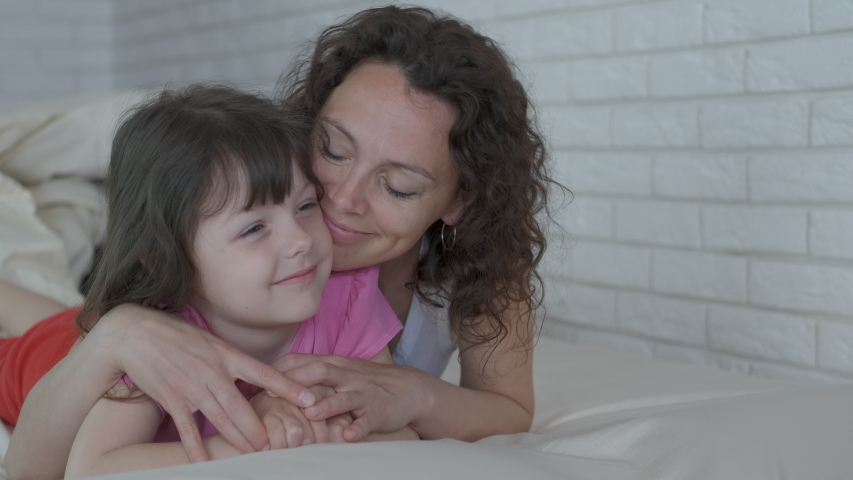 Woman with a child in the bedroom. Happy mother hugs daughter in bed. | Shutterstock HD Video #1038367421