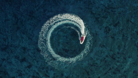 Slowmotion aerial shot of a fast speedboat with a red roof top driving around in the circle and making beautiful doughnuts in the clear turquoise magical sea. Top travel destination. 4K. 