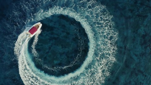 Slow motion aerial shot descending towards fast speedboat with a red roof top, going around in the circle and making beautiful shapes in the clear sea. Top travel destination. 4K.