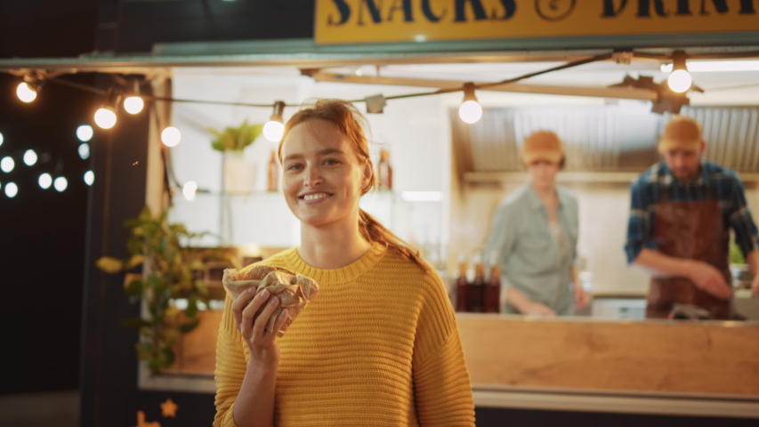Beautiful Young Female Walks Away from a Food Truck with a Delicious Fresh Beef Burger. She's Happy with Hew Food and Takes a Biet. Commercial Kiosk is Selling Street Food on a Modern Cool Street. | Shutterstock HD Video #1038373991