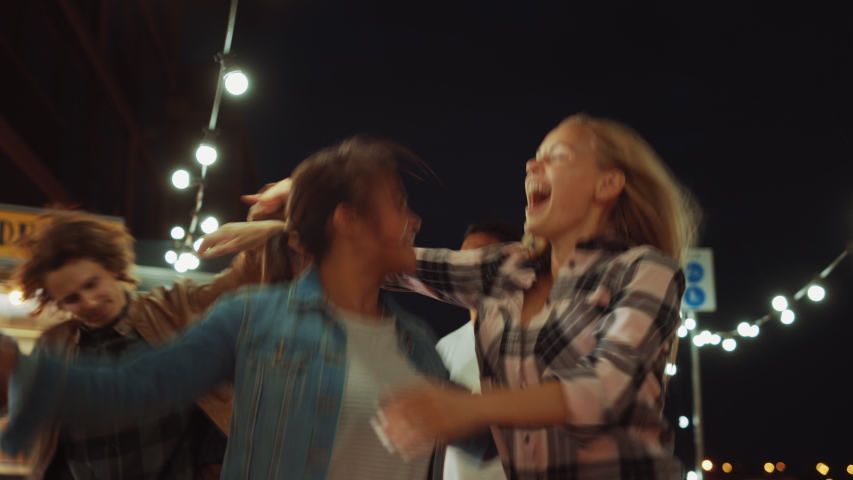 Group of Friends are Having a Party Outside a Street Food Burger Cafe. Two Beautiful Girls Hugging and Dancing to Music. It's Evening in a Modern Neighbourhood. Everybody are Happy and Full of Joy. | Shutterstock HD Video #1038374018