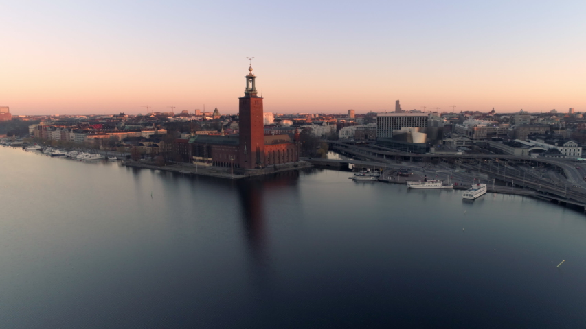 Aerial view of Stockholm City Hall and cityscape at sunrise. Drone shot flying over Riddarfjärden water, small harbor and bridges in the background. Town Hall, Stadshuset Skyline, Capital of Sweden Royalty-Free Stock Footage #1038378929