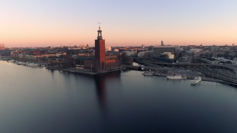 Aerial view of Stockholm City Hall and cityscape at sunrise. Drone shot flying over Riddarfjärden water, small harbor and bridges in the background. Town Hall, Stadshuset Skyline, Capital of Sweden