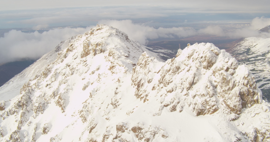Aerial helicopter shot, track past Alaskan mountain peak, zoom in on the city of Anchorage through the clouds, drone footage