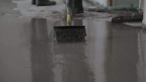 Rolling cement to form a smooth, even surface on floor. Man in rubber boots using roller to flatten poured concrete in building site. Close up.