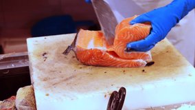 Hands of fishmonger processing fresh raw salmon, preparing fish fillet for sale in shop