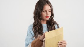 Upset brunette girl in sweater sadly opening envelope with exam results over white background