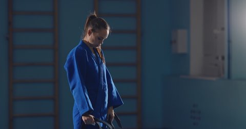Young girl fighter is preparing for a training session, tying a belt in a kimono. Judo training.