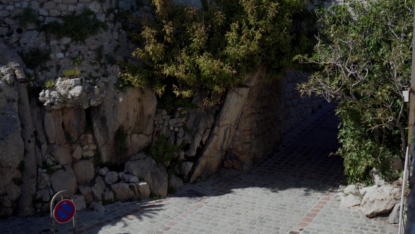 Young happy woman in red romantic polka-dot dress running into the ancient, stone arch overgrown with greenery. Antibes, France. Top view